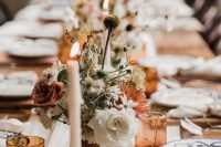 lovely boho fall wedding centerpieces of dried and fresh blooms in white and rust, dried greenery and with candles and berries on the table