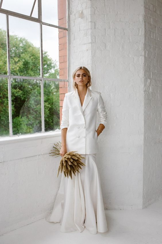 a chic and minimalist bridal look with an oversized white blazer and a maxi pleated skirt plus a grass wedding bouquet and statement earrings