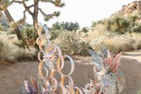 10 a chic iridescent wedding altar of rings, with bright grasses, fronds, leaves and blooms on acrylic stands is a very fresh idea