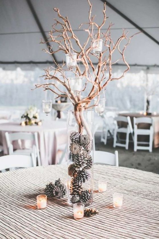 a frosty winter wedding centerpiece of a tall vase with pinecones and branches with candleholders plus more candles around