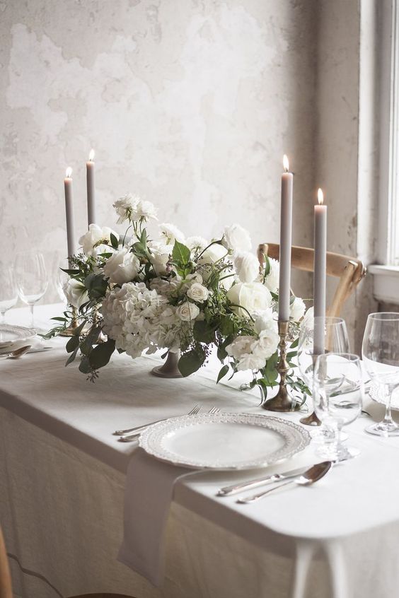 a light and ethereal refined winter wedding tablescape with grey candles and napkins, all white everything and white blooms and greenery