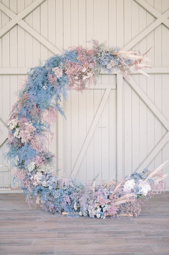 an iridescent half moon wedding backdrop covered with white, pink and blush blooms and pampas grass all over