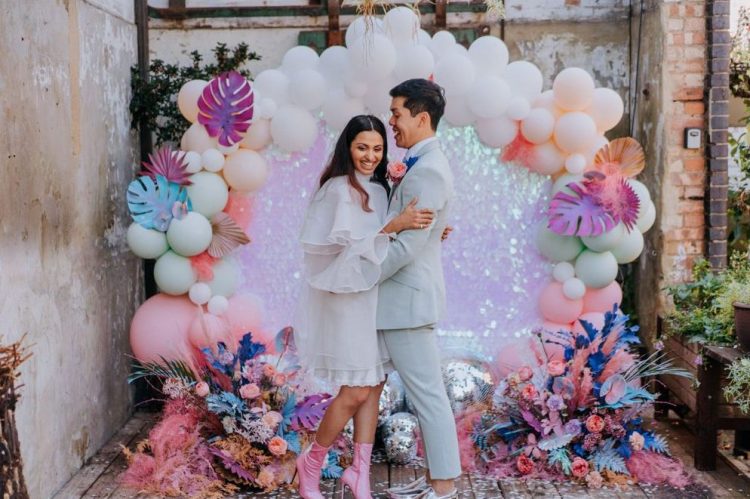 a jaw-dropping wedding backdrop covered with pink iridescent sequins, with spray painted fronds, blooms and balloons is breathtaking