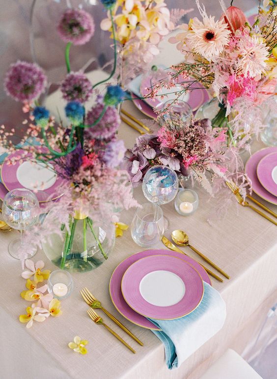 a super bright iridescent wedding table setting with pink, yellow and purple blooms, blue touches and gold