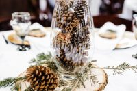 24 a simple rustic winter wedding centerpiece of a wood slice, a tall glass with pinecones and evergreens is veyr easy and fast to DIY