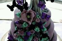 26 a statement lilac wedding cake with green, purple and lilac blooms, black butterflies and Jack and Sally cake toppers