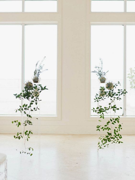 a beautiful minimalist wedding altar of acrylic stands with cascading greenery and some potted plants is an ethereal and serene idea for a spring wedding
