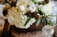 a beautiful rustic wedding centerpiece of wood slices, a wooden box with white roses, hydrangeas, seed pods, cotton and greenery
