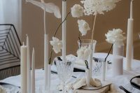 a bold and edgy minimalist wedding tablescape with neutral linens, black chargers and cutlery, neutral candles of various sizes and white blooms