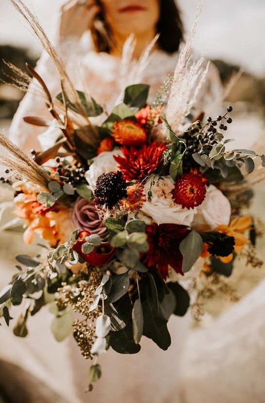a bold fall wedding bouquet that includes burgundy, deep red, dusty pink, white and yellow blooms, greenery, grasses and privet berries