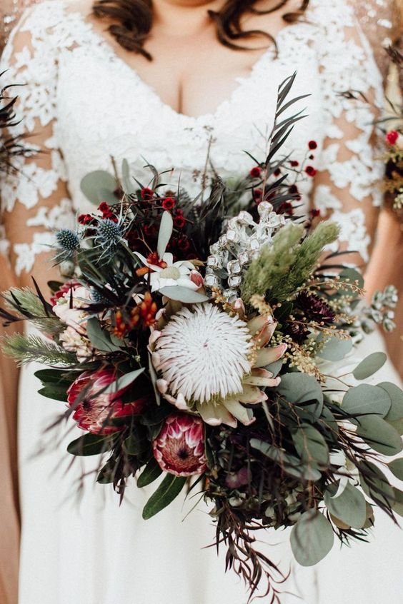 a bright fall wedding bouquet of pink and white king proteas, greenery and dark foliage, berries, thistles and various textural elements is wow