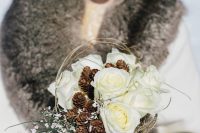 a catchy winter wedding bouquet of white roses, pinecones and small white blooms, twigs and a vine wrap is all cool