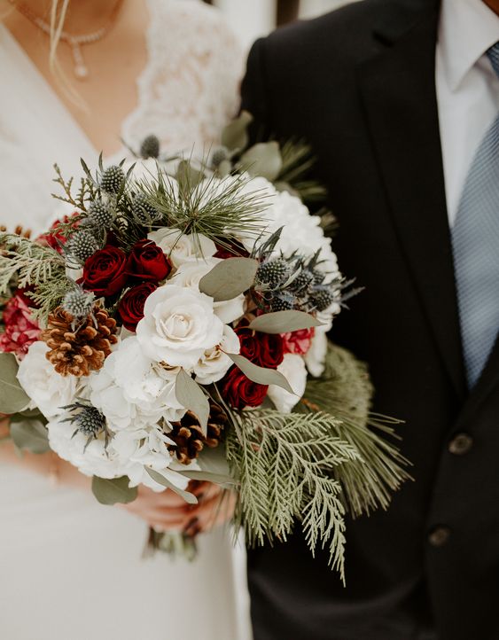 a classic winter wedding bouquet of white and red roses, evergreens, thistles, pinecones and greenery is timeless for a winter bride