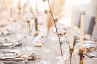 a cluster wedding centerpiece of a cotton branch, some dried blooms, thin and tall candles is a cool solution for a boho wedding