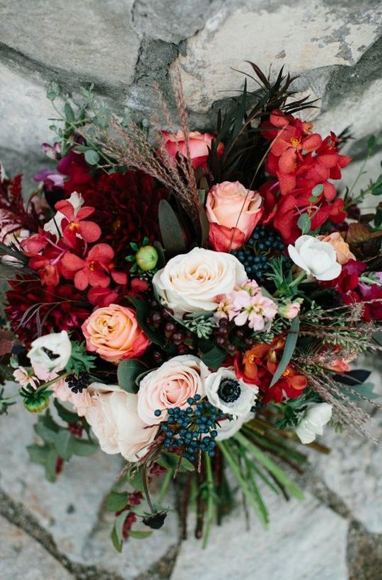 a colorful fall wedding bouquet of burgundy and deep red blooms, white and blush ones, various berries, foliage and grasses is super cool