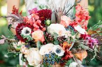 a colorful fall wedding bouquet of white, deep red, fuchsia, orange and yellow blooms, greenery and cascading touches, grasses and berries