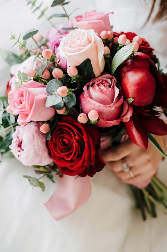 a colorful wedding bouquet of deep red and pink roses and peonies, of berries and eucalyptus is amazing for a summer wedding