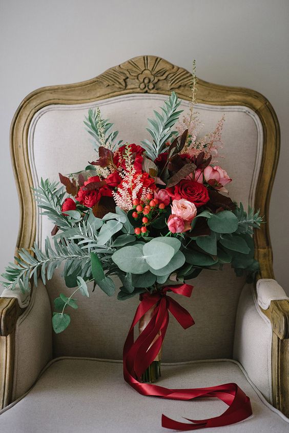 a colorful wedding bouquet of red and pink blooms, berries and various types of greenery for a Christmas wedding