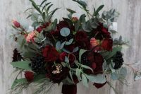 a dark wedding bouquet of burgundy and deep red blooms, berries and lots of textural greenery is great for both moody fall and winter weddings