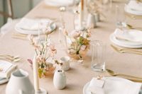 a delicate minimalist wedding tablescape with a blush tablecloth, blush blooms and greenery, neutral and rust candles, white plates and napkins, gold cutlery