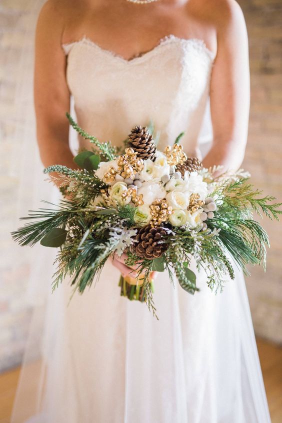 a glam and shiny winter wedding bouquet of white blooms, gilded berries, pinecones, evergreens and greenery is a lovely idea