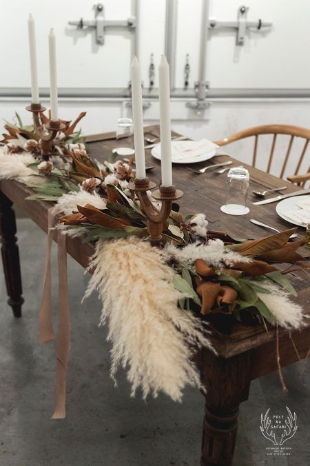 a gorgeous boho wedding table runner of magnolia leaves, pampas grass, cotton, with thin tall candles and with ribbons is super chic