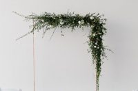 a gorgeous minimalist wedding arch decorated with lush greenery and white blooms plus a colorful rug is a cool and fresh idea