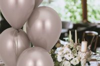 a greige floral print tablecloth, greige balloons, white blooms, white pilalr candles and greenery and white porcelain are chic