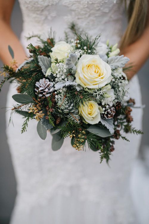 a lovely snowy winter wedding bouquet of white blooms, pale greenery, evergreens, pinecones, baby's breath and twigs is amazing