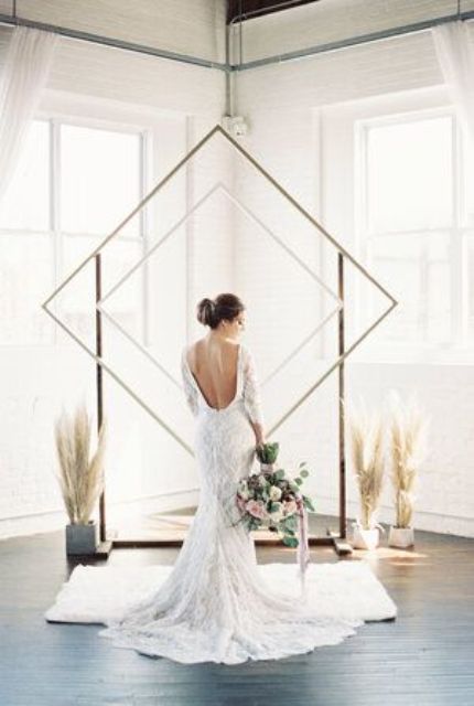 a minimalist double rhomb wedding arch and arrangements of pampas grass in vases around it for a minimalist boho wedding