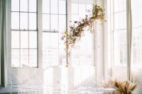 a minimalist fall wedding altar of bold fall leaves hanging over the space and some pampas grass on the floor plus ghost chairs