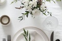 a minimalist neutral wedding tablescape with a neutral floral centerpiece, neutral plates, black cutlery, candles and a striped napkin