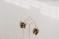 a minimalist wedding ceremony space with a geo wedding arch with pink floral arrangements, ghost chairs and pillar candles lining up the aisle