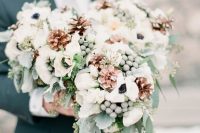a pretty and lush winter wedding bouquet of white blooms, pale greenery, berries, pinecones is a cool idea for a winter wedding