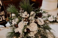 a pretty winter wedding bouquet of white blooms, evergreens, berries, pinecones is a lush and very textural idea for a rustic celebration