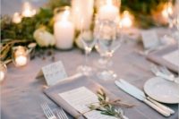 a refined greige wedding tablescape with a greenery runner, pillar candles, a greige napkin, white plates and cutlery