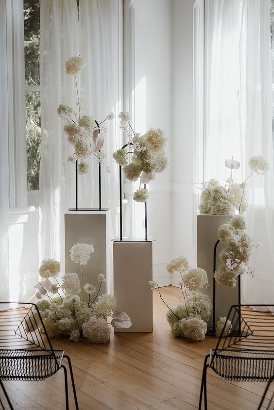 a refined minimalist wedding altar of tall white stands with tall white floral arrangements is a gorgeous idea for a delicate minimal wedding