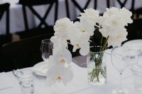 a refined minimalist wedding tablescape with crispy white linens, white roses and rochids, white plates and black menus