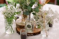 a relaxed cluster wedding centerpiece of vases and bottles with greenery, baby’s breath, cotton and some candles around is chic