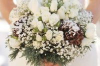 a snowy winter wedding bouquet of white baby’s breath, white roses, evergreens and pinecones is a cool solution for winter