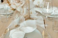 a subtle and chic greige wedding tablescape with a greige woven placemat and matching plates, white napkins and a table runner, neutral blooms and greige candles