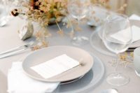 a subtle greige wedding tablescape with a greige tablecloth and plates, with bold blooms and greenery, white cutlery is a lovely idea for fall