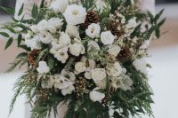 a super lush white wedding bouquet of blooms, greenery, fern, pinecones and long emerald ribbons is amazing for winter and can be rocked in the fall