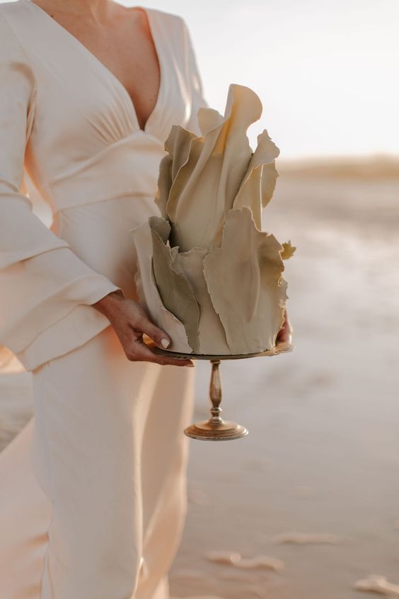 a unique greige wedding cake covered with sugar shards that imitate fabric flowing in the wind is a fantastic idea to rock