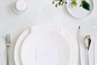 a white all-minimalist wedding tablescape with all white everything, some greenery to refresh the look and candles