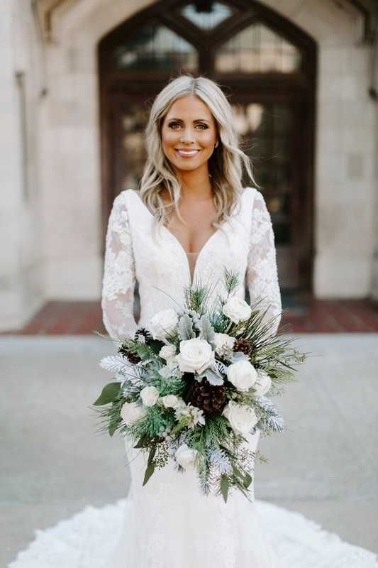 a white winter wedding bouquet of white blooms, pale leaves and greenery and pinecones is a perfect solution for a winter glam bride