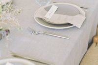 an airy minimalist wedding tablescape with a grey tablecloth, plates and napkins, dried blooms and candles is a stylish idea