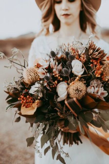 an earthy colored textural boho wedding bouquet of rust, white and pink blooms, greenery, thistles and berries is cool for a boho wedding