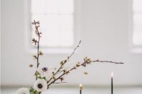an elegant minimalist wedding table setting with neutral plates, grey napkins, white blooms, thin and tall black candles