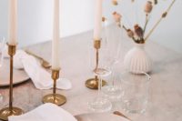 an elegant minimalist wedding tablescape with a marble table, tall and thin candles, dried blooms, gold cutlery and gold candlesticks